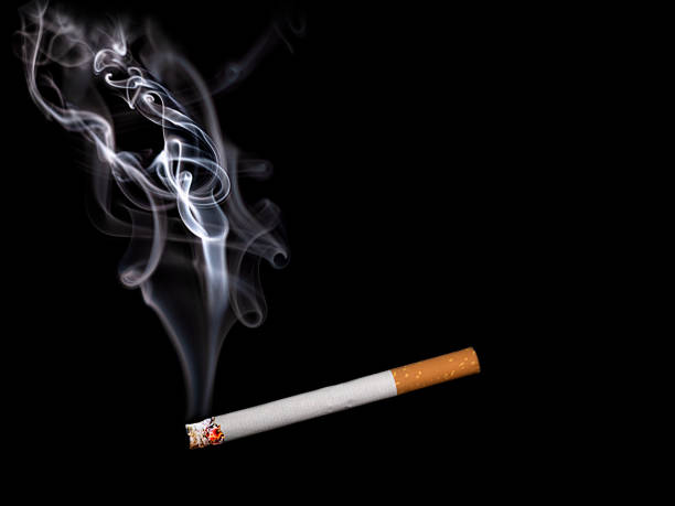 istock Close up of a cigarette with smoke showing at black background 1180214657