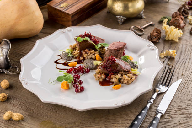 Deer chops with pearl barley and cranberry sauce on wooden table side view