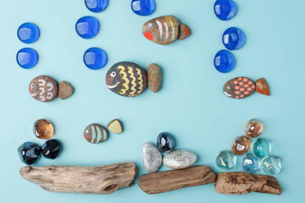 Diy painted stone fish on blue background and sea decoration. Creative DIY idea, surreal imagination kids world. Kid handmade, kindergarten, daycare concept.