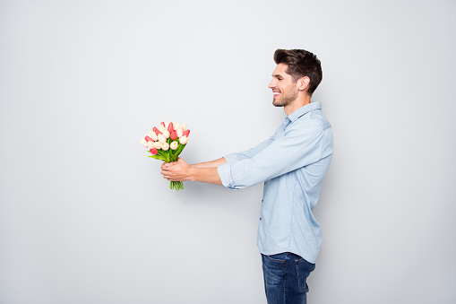 Profile side photo of positive cheerful man lover have fun give tulips bouquet to his girlfriend on 8-march 14-february date copyspace, have fun wear stylish clothes isolated over grey color background
