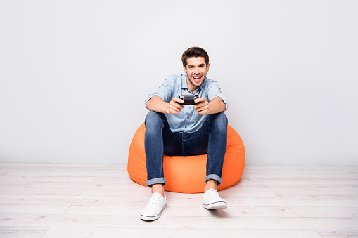 Full length body size photo of trendy man addicted to playing video games, wearing white sneakers holding joy stick with hands isolated over grey color background