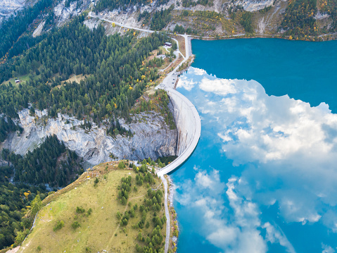 Water dam and reservoir lake in Swiss Alps to produce hydropower, hydroelectricity generation, renewable energy, aerial drone photography