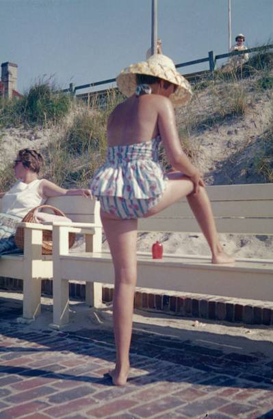young woman is protecting herself with sunscreen from a sunburn by the sea - image created 1960s 1960s style beach women imagens e fotografias de stock