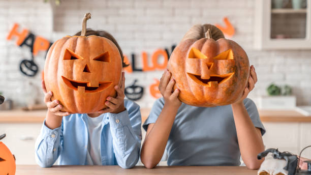 due bambini piccoli che festeggiano halloween in cucina - halloween pumpkin party carving foto e immagini stock