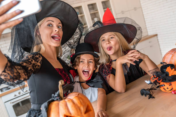 nahaufnahme von glücklichen jungen frau, die selfie und spaß mit ihren kindern in halloween dekoriert küche - costume expressing positivity cheerful close up stock-fotos und bilder