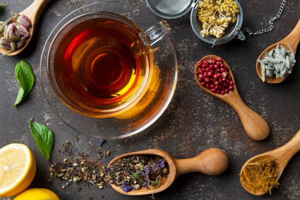 Herbal Tea Directly above view of a tea cup with herbal tea and flowerhead of a camomile. Surrounded by a variety of herbal teas and tea ingredients like Chamomile tea, Sage tea, Linden tea, Fennel tea, Melissa tea,Red pepper, Rose tea, Rosemary Tea , Corn silk tea , anise, cinnamon, thyme, mint, ginger, fresh lemon and rosemary on wooden background. rose tea stock pictures, royalty-free photos & images