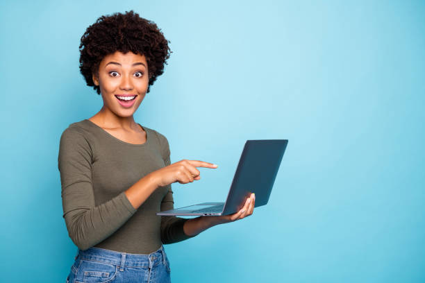 photo of cute stylish trendy black model pointing at laptop recommending you to purchase it requesting to follow on social media wearing hreen sweater jeans denim isolated vivid color blue background - job joy student computer imagens e fotografias de stock