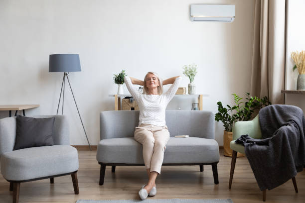 relaxed older woman sitting on couch in air conditioner room - confortável imagens e fotografias de stock