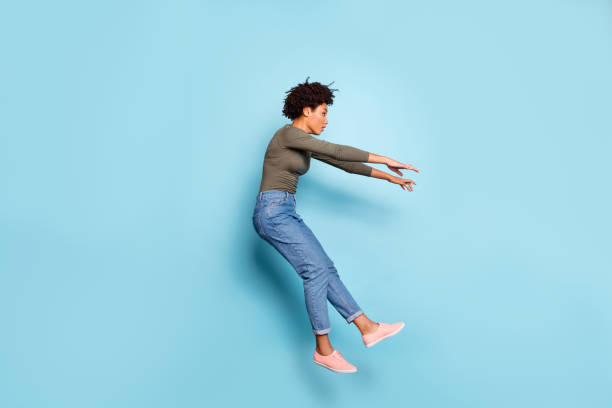 Oh my god. Full length photo of dark skin wavy lady jumping high blown away by strong stormy wind confused wear casual outfit isolated pastel blue color background Oh my god. Full length photo of dark skin wavy lady jumping high blown, away by strong stormy wind confused wear casual outfit isolated pastel blue color background zero gravity stock pictures, royalty-free photos & images