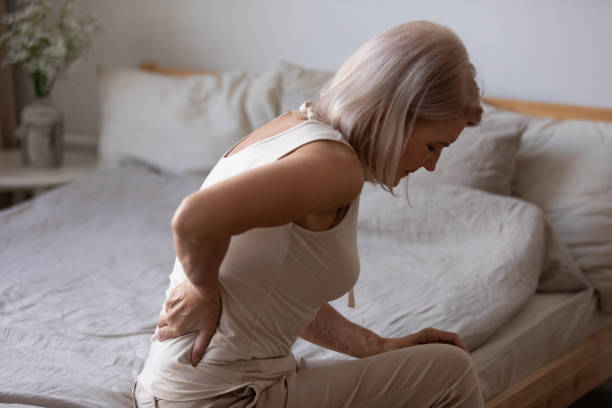mujer madura molesta que sufre de dolor de espalda, frotando los músculos rígidos - colchones fotografías e imágenes de stock