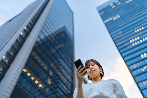 A Young woman is using a smart phone in front of tall skyscrapers.