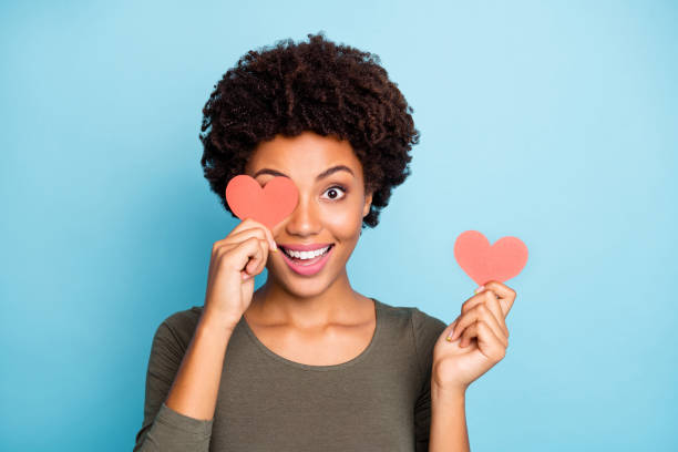 close up photo of amazed excited emotions expression afro american girl hold little paper card close cover her face have fun on date for 14-february wear green sweater isolated over blue color background - fashion model small one person happiness imagens e fotografias de stock