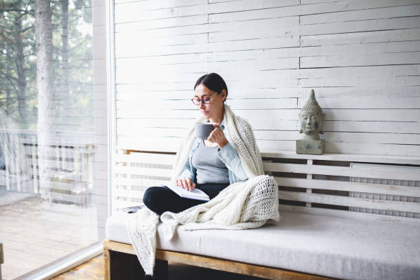 middle-aged woman siting comfortable and reading a book - winter women zen like photography imagens e fotografias de stock