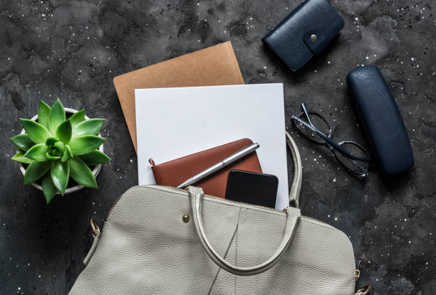 istock Women's bag with office accessories on a dark background, top view 1180237963