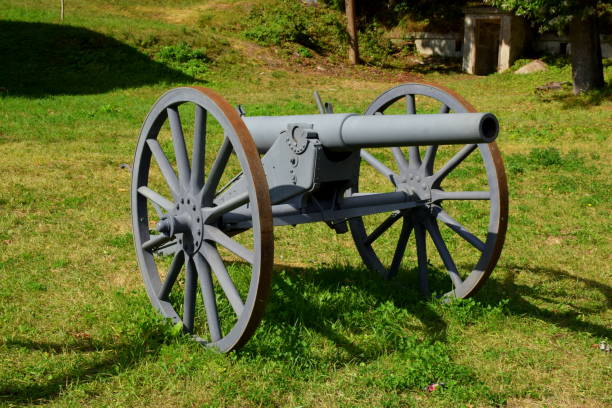 istock Single massive grey cannon replica on two rusty wheels with base and barrel  visible stanting next to an ad hoc wooden barricade in the middle of a lush field, pastureland, or meadow seen in Poland 1180239962
