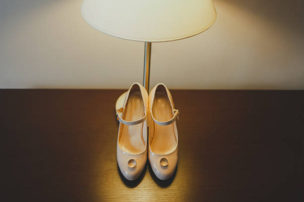 istock Wedding attributes concept. Wedding rings lie on the bride’s shoes and are illuminated by a table lamp 1180244531