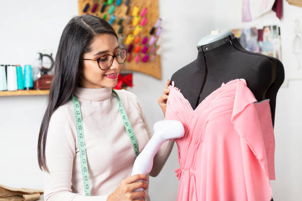 istock Hispanic fashion designer in her studio with a steam iron working on her designs- enterprising woman 1180246181