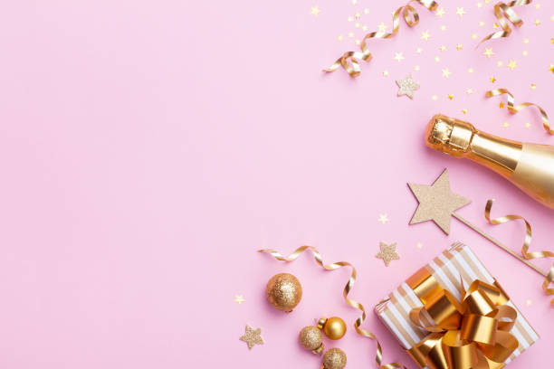 istock Modern Christmas or New year festive background. Champagne bottle, gift or present box and golden confetti on pink top view. Flat lay. 1180246283