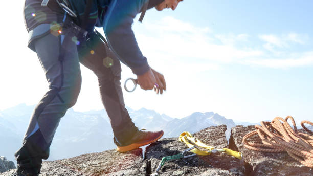 istock Mountaineer places gear on rock summit, for rope safety 1180248401