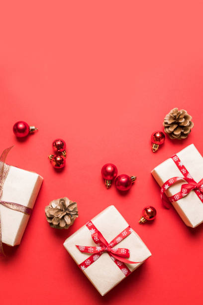 istock Christmas composition with red present box, ribbons, red big and small balls, brown cones holiday decorations on a red background. 1180253384