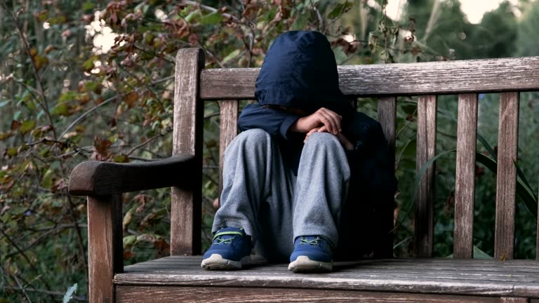 Crying child boy sitting on a bench covering his face