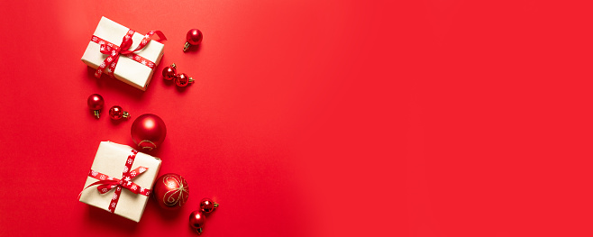 Christmas composition with festive red craft boxes and red ribbons and small balls on red background. Flat lay, top view, copy space. Minimal New Year concept.