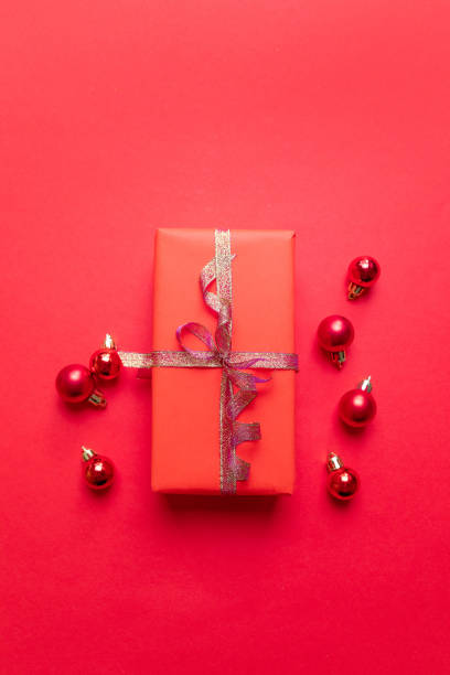 istock Creative Christmas composition with red present box, ribbons, red big and small balls, holiday decorations on red background. Flat lay, top view, copy space 1180257232