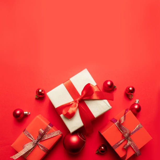 istock Creative Christmas composition with red present box, ribbons, red big and small balls, holiday decorations on red background. Flat lay, top view, copy space 1180257237