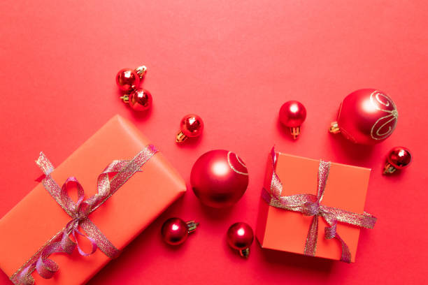 istock Christmas composition with red present box, ribbons, red big and small balls, holiday decorations on red background. 1180257255