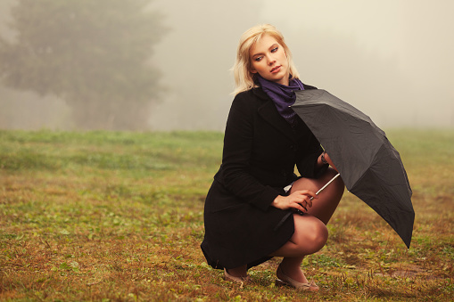 Young fashion woman with umbrella in a fog Stylish female model in classic black coat outdoor