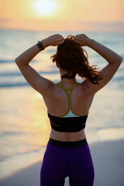 Photo of fit sports woman on seacoast at sunset adjusting hair