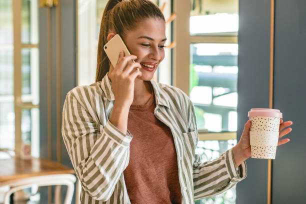 istock Young woman holding phone and coffee 1180263765