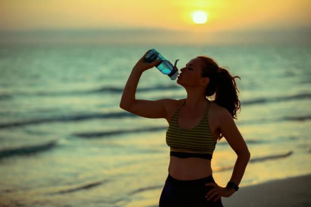 istock fit woman on beach at sunset drinking water from bottle 1180265046