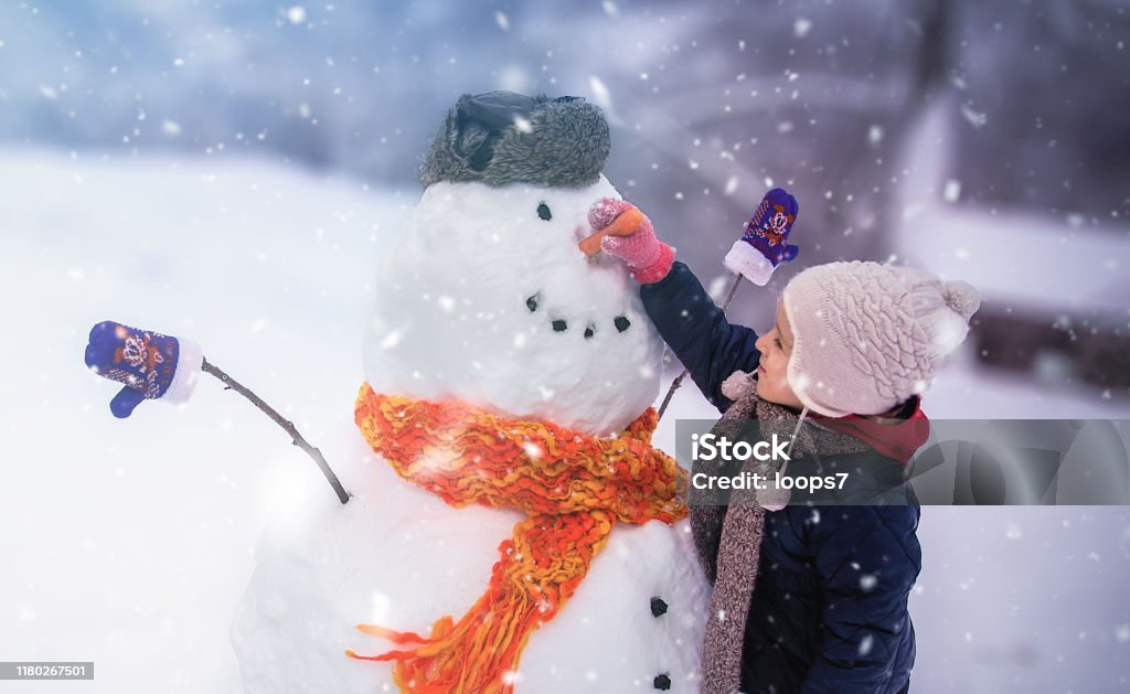 Child Winter Outdoor Fun Child sculpts a snowman in a park Child Stock Photo