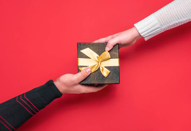 Christmas giving gift concept. Xmas gift box. Giving presents Giving and receiving festive gift box. Christmas gifting time concept. Man and woman hands on a black gift box on red background. Xmas gift exchange. gift lounge stock pictures, royalty-free photos & images