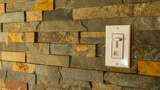 A plastic light switch on a stylized stone wall features both a dimmer slider and an on/off switch.