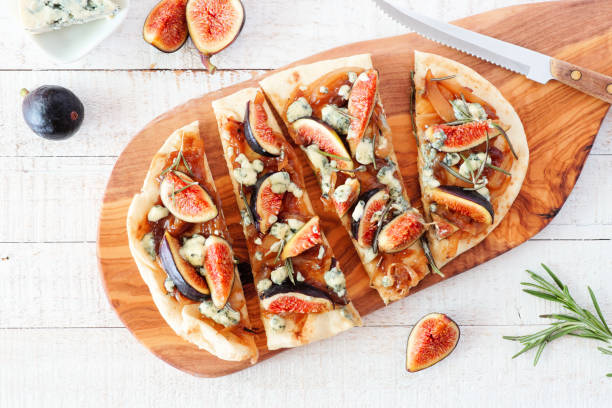 Autumn flat bread pizza with figs, caramelized onions, blue cheese and rosemary, top view table scene on white wood Autumn flat bread pizza with figs, caramelized onions, blue cheese and rosemary. Top view table scene on a white wood background. flatbread stock pictures, royalty-free photos & images