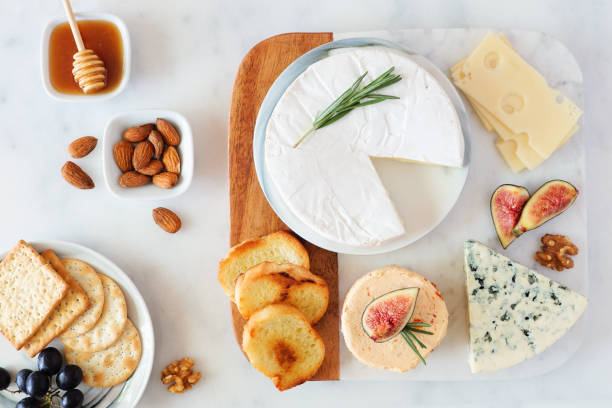 Cheese platter with a selection a cheeses, crackers, figs, nuts and honey, overhead table scene on a marble background Cheese platter with a selection a cheeses, crackers, figs, nuts and honey. Overhead table scene on a bright background. brie stock pictures, royalty-free photos & images