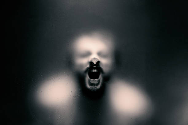 istock Creepy looking man is screaming behind a frosted glass. 1180276451