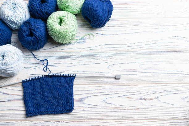 istock Knitting in progress. Flat lay composition with blue and green yarn and needles on white wooden background. 1180276730