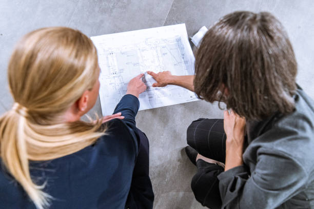 istock Two women looking and pointing at blueprints 1180281959