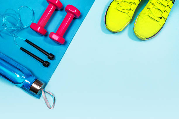 Athlete's set with pink dumbbells, bottle of water, jump rope on blue yoga mat and yellow sneakers on pastel blue background. Athlete's set with pink dumbbells, bottle of water, jump rope on blue yoga mat and yellow sneakers on pastel blue background. Flat lay, top view, copy space. exercise equipment stock pictures, royalty-free photos & images