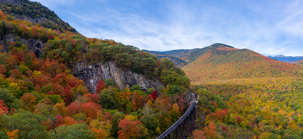 Autumn fall colors in Crawford Notch State Park. HDR drone pano shot with train tracks in foreground with forest stretching into distance and up mountains.