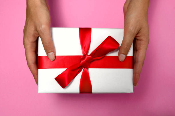 Gift in female hands on a colored background top view. gift box in women's hands flat lay. Female hands holding present with red bow. Festive backdrop for holidays: Birthday, Valentines day, Christmas regalo en manos femeninas en una vista superior de fondo de color. caja de regalo en las manos de las mujeres plana lay. manos femeninas que sostienen la presente con lazo rojo. telón de fondo festivo para las vacaciones: cumpleaños, día de san valentí