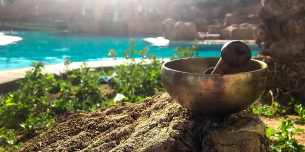 Tibetan singing bowl in the sun on the background of the water is charged with solar energy. Alternative medicine in yoga for balance and sound therapy. Tibetan singing bowl for sound therapy and yoga