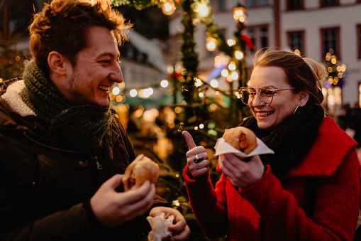 Young man and woman eating hot dogs on Christmas market