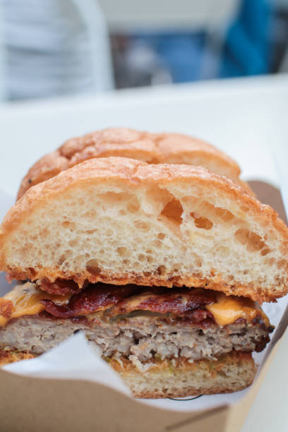 istock Delicious last-minute gourmet hamburger cut in half with cheddar bacon with small tomatoes Classic american fast food background. Cut in half burgers with grilled meat and onions on wood. Hamburgers with fresh vegetables on craft wrapping paper 1180321053