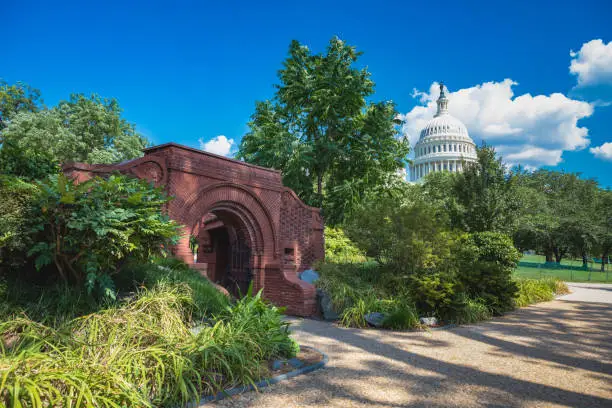 Summerhouse on the grounds of Capitol Hill in Washington, DC. The open brick structure was designed by famous architect Frederick Law Olmsted around 1880 to serve as a rest stop and drinking fountain for travelers. In the background is the US Capitol dome.