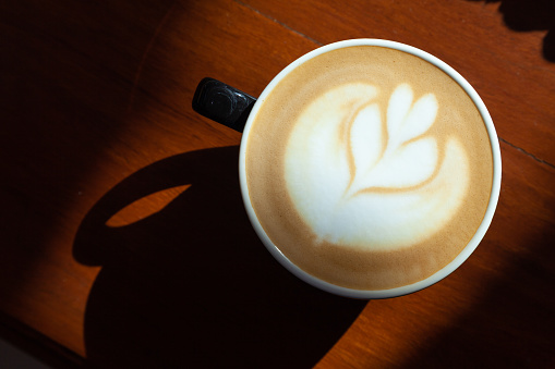 Top view of coffee latte art with tulip pattern on top on rustic wooden table bar in morning light with copy space
