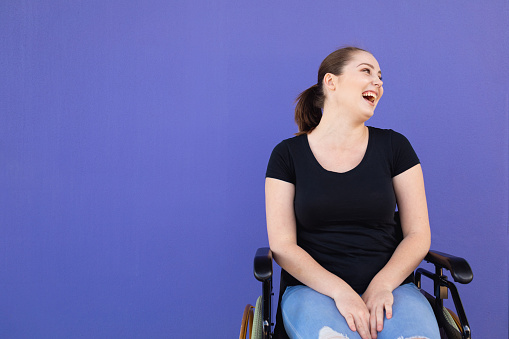 Confident Young Disabled Woman In Wheelchair Against Purple Background